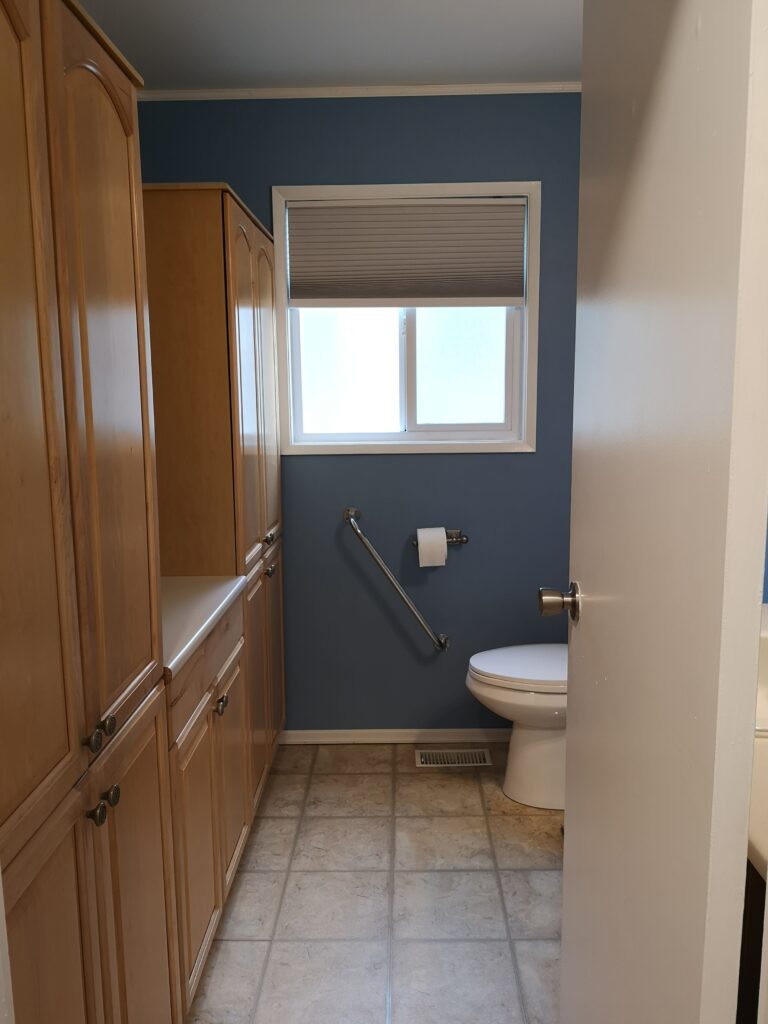 A bathroom with a window, toilet and large cabinetry before renovation. 